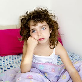 A young girl sitting up in bed looking defeated because she has lice